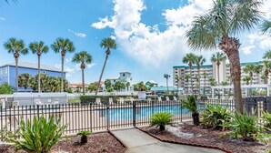 A pool area with palm trees, a fence, and buildings in the background.