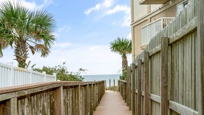 A wooden boardwalk leading to a beach, flanked by palm trees and a white fence.