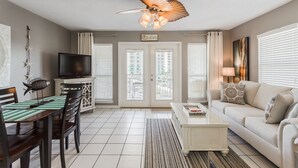 A living room with a television, a dining area with chairs and a table, a white sofa, and a ceiling fan.