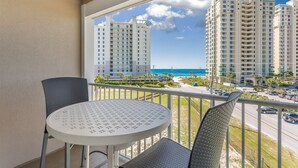 A balcony with a round table and two chairs, overlooking a beach and high-rise buildings.