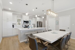A modern kitchen with white cabinetry, a central island, bar stools, and pendant lighting.