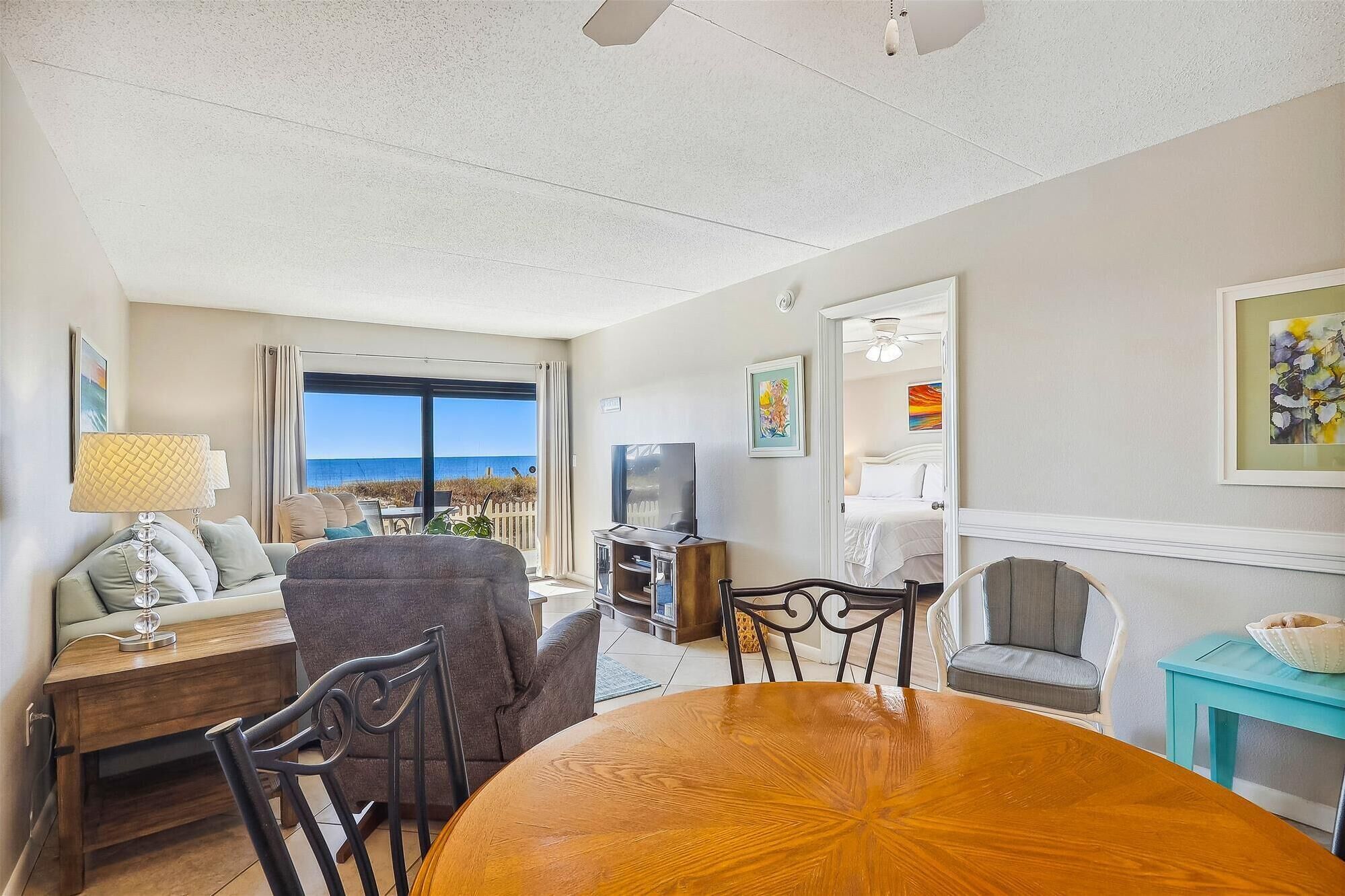 A living room with a wooden dining table, a sofa, a TV, and a view of the ocean.