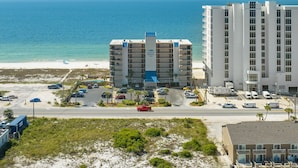 A beachfront hotel with multiple floors, a parking lot, and a view of the ocean.