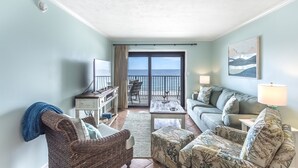 A living room with a view of the ocean, a sofa, a chair, a coffee table, and a TV.