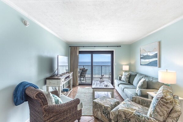 A living room with a view of the ocean, a sofa, a chair, a coffee table, and a TV.