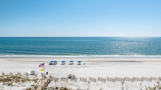 A beach with a wooden boardwalk leading to beach umbrellas and a lifeguard station.