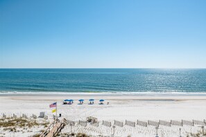 Een strand met een houten looppad dat leidt naar strandparasols en een redderstation.