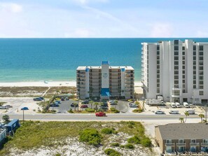 A beachfront hotel with multiple floors, a parking lot, and a view of the ocean.