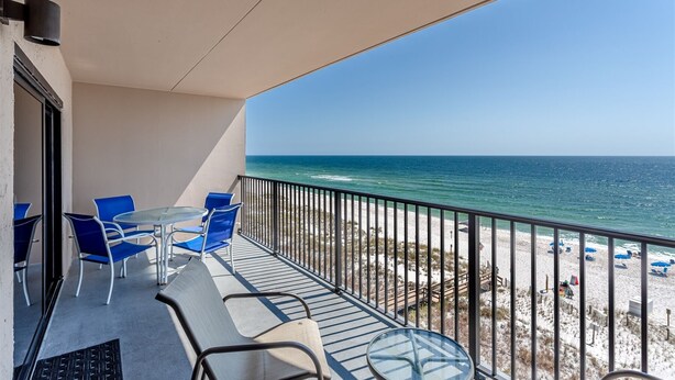 A balcony with a table and chairs, a view of the beach and ocean.