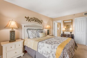 Une chambre à coucher comprenant un lit, deux tables de chevet avec des lampes, une commode, un miroir et une porte.