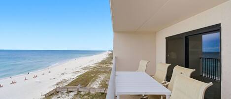 A balcony with a table and chairs overlooking a beach.