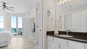 A bathroom with a large mirror, white cabinets, a sink, and a ceiling fan.