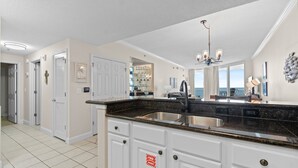 A kitchen with white cabinets, a granite countertop, and a view of the ocean.