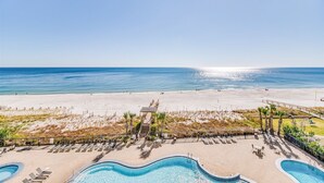 A beach resort with a swimming pool area, sun loungers, and a view of the ocean.