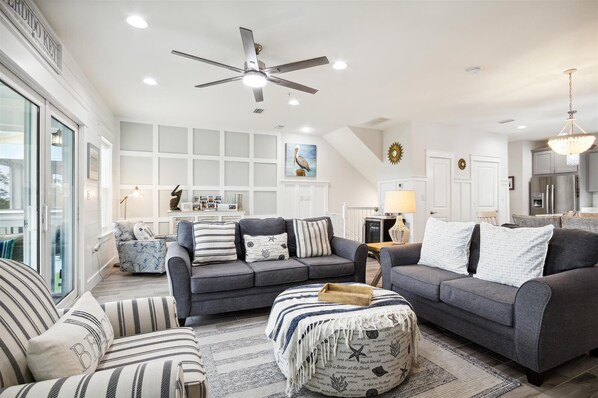 A modern living room with grey sofas, striped cushions, and a ceiling fan. - NEW LISTING! Lost Key Golf & Beach Club ~ Pelicans Paradise - NO HASSLE CHECK OU (Perdido Key)
