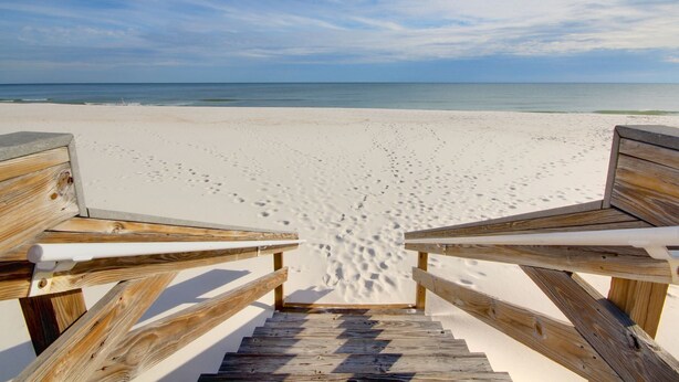 Een houten trap die naar een strand leidt, met voetafdrukken in het zand.