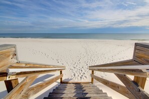 Eine Holztreppe führt zu einem Strand, im Sand sind Fußabdrücke zu sehen.