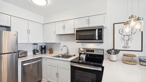 Een moderne keuken met witte kasten, roestvrijstalen apparatuur, een magnetron, een waterkoker en een spoelbak.
