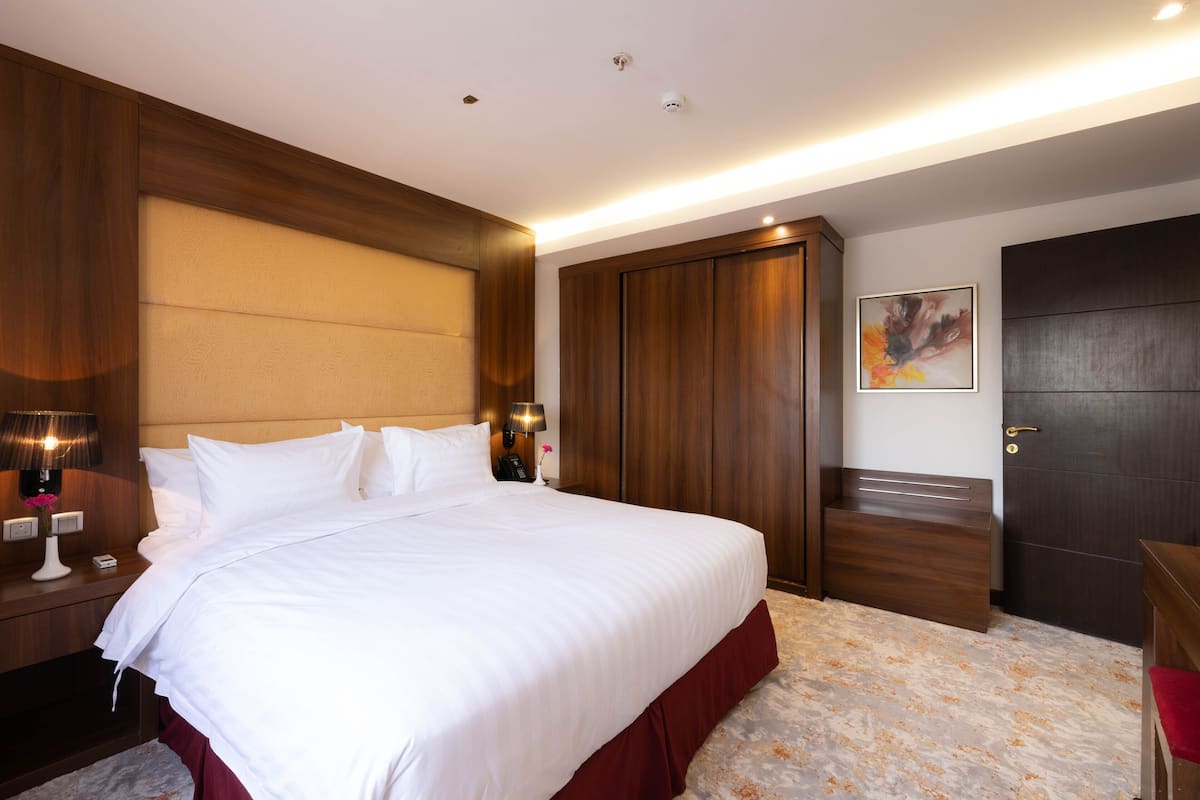 A large bed with white linens, a wooden headboard, and a nightstand with a lamp.