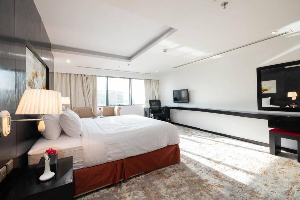 A hotel room with a large bed, a desk, a TV, and a window with curtains.