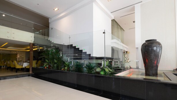 A modern hotel lobby with a glass staircase, a large vase, and indoor plants. - MIRA BUSINESS HOTEL (Riyadh)