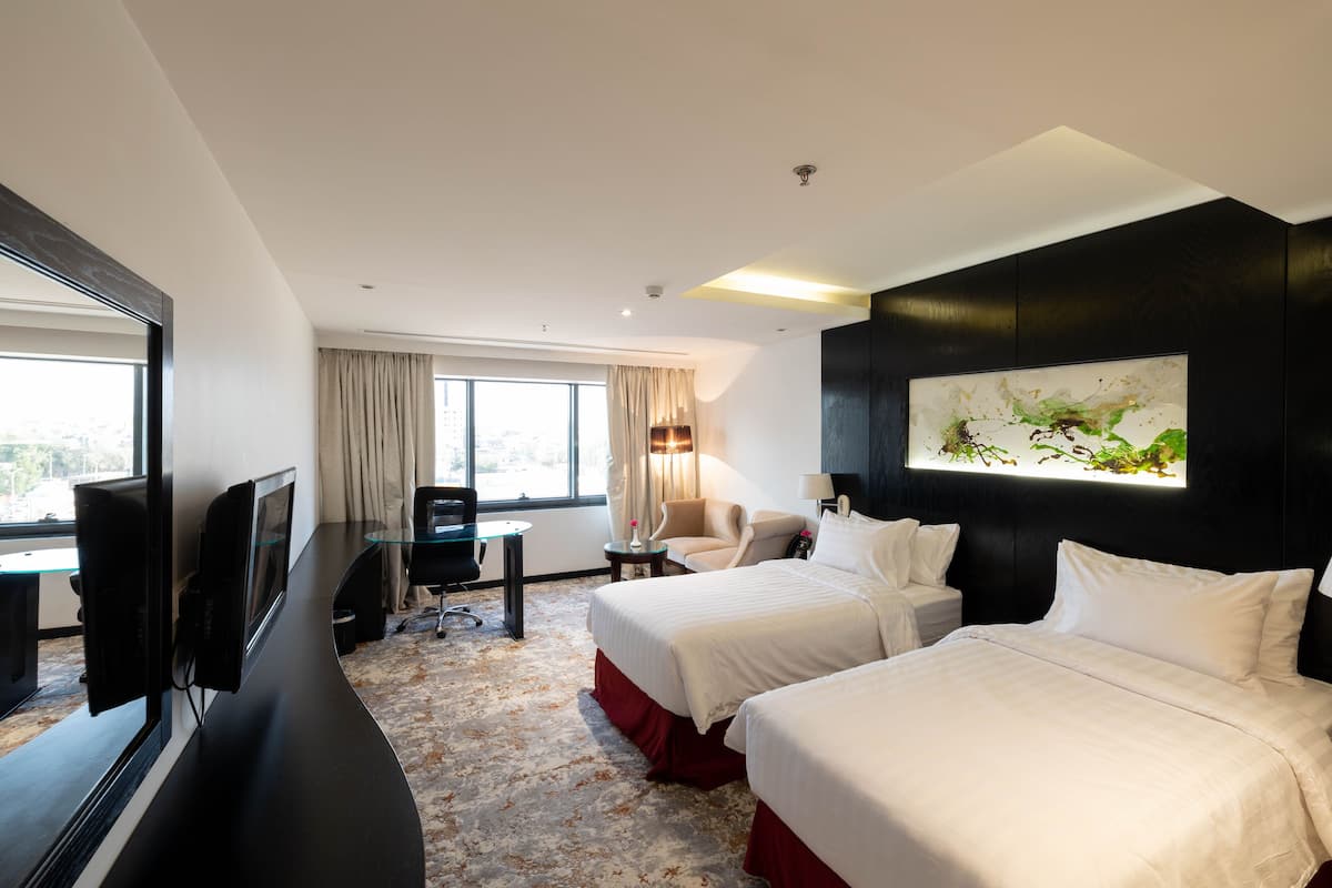A hotel room with two beds, a desk with a chair, a TV, and a large window with curtains.