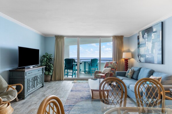 A living room with a television, seating, a dining table, and a view of the ocean.