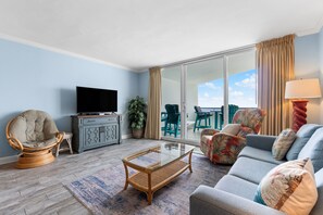 A living room with a flat-screen TV, a glass coffee table, a sofa, and a chair.