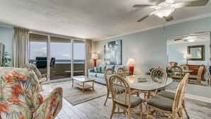 A spacious living area with a balcony, a dining table with chairs, and a ceiling fan. - Perdido Sun 1004 - indoor pool - Beachfront - NO HASSLE CHECK OUT (Perdido Key)
