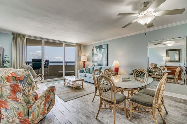 A spacious living area with a balcony, a dining table with chairs, and a ceiling fan.