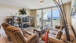 Ein Wohnzimmer mit einer Couch, Fernseher und einem Balkon mit Meerblick.