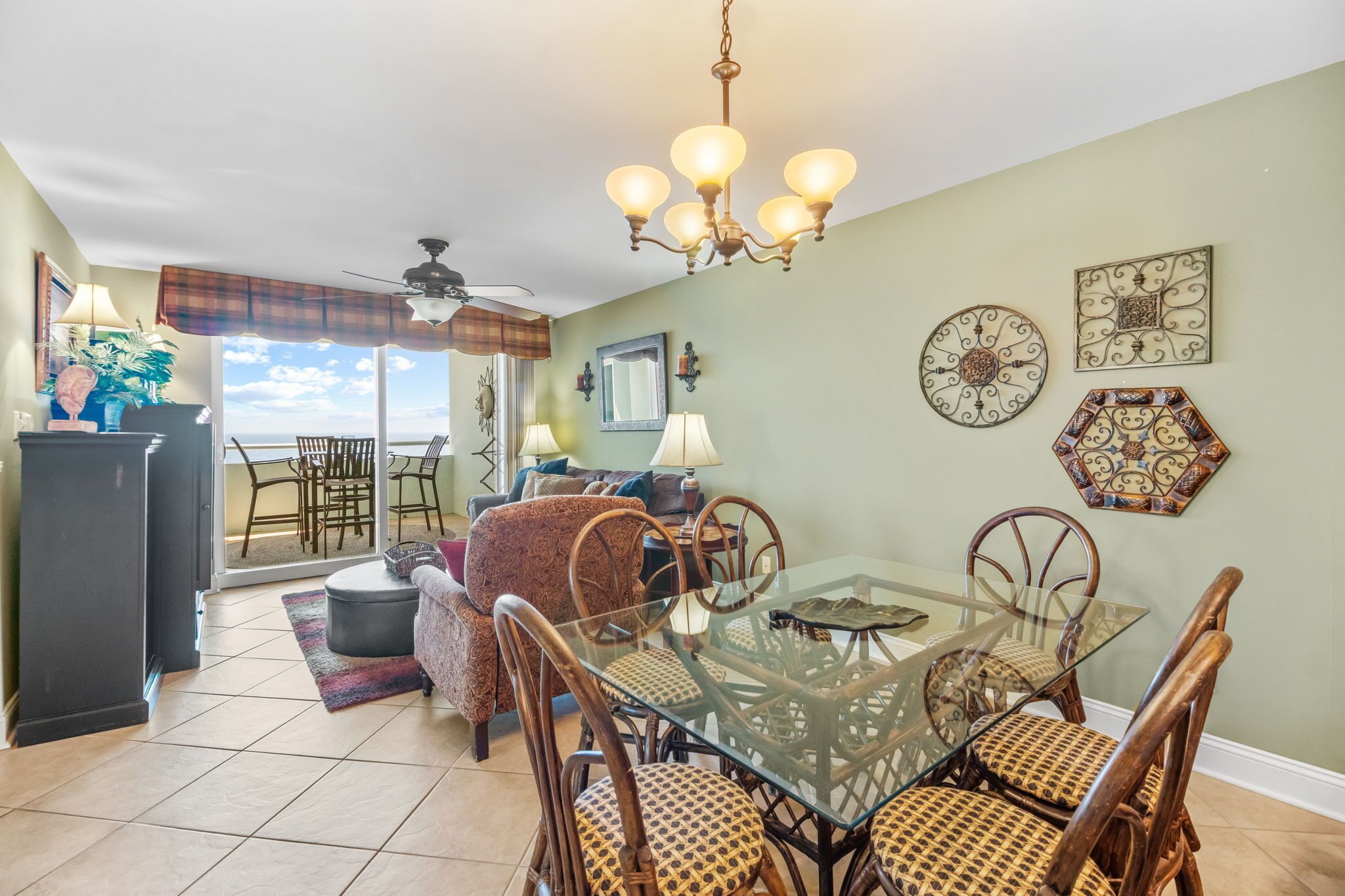 A dining area with a glass table and wooden chairs, a ceiling fan, and decorative wall art.