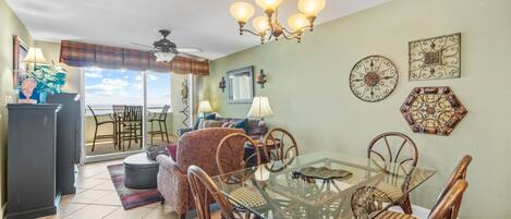 A dining area with a glass table and wooden chairs, a ceiling fan, and decorative wall art.