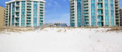A beachfront hotel with a curved facade, multiple balconies, and a sandy beach in the foreground.