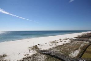 A beach with a wooden boardwalk leading to the water, a sandy shore, and a clear sky.