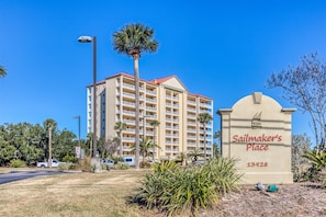 Een meerlaags hotel met een rood dak en balkons, een bord met de tekst 'Sailmaker's Place 13928', en een palmboom op de voorgrond.