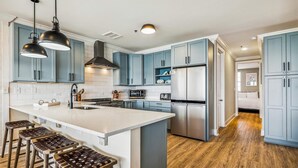 A modern kitchen with light blue cabinets, a central island with stools, stainless steel appliances, and pendant lighting. - SAILMAKER 1001 - Ole River Views -NO HASSLE CHECK OUT (Pensacola)