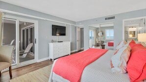 A bedroom with a large bed, a dresser, a TV, and a sliding glass door leading to a balcony.