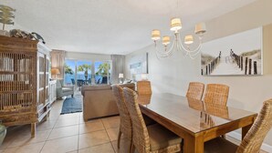 A spacious living area with a dining table, wicker chairs, and a chandelier. - Sandy Key 227 Second floor -Beachfront view -NO HASSLE CHECK OUT (Pensacola)