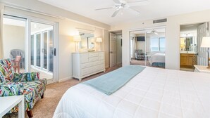 A hotel room with a large bed, a dresser, a chair, a mirror, and a ceiling fan.