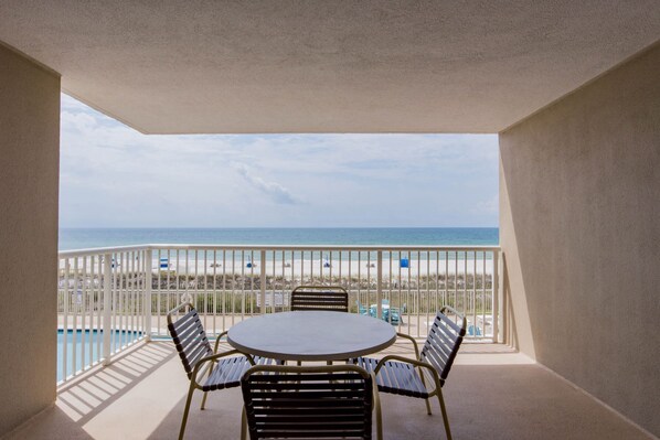 A balcony with a round table and four chairs, overlooking a beach with a fence and beach chairs. - Sandy Key 235 Second floor -Beachfront view -NO HASSLE CHECK OUT (Pensacola)