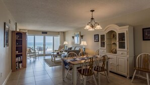 A spacious living area with a dining table, chairs, a sofa, and a view to the outside. - Sandy Key 235 Second floor -Beachfront view -NO HASSLE CHECK OUT (Pensacola)