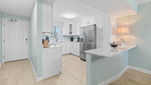 A modern kitchen with white cabinets, a stainless steel refrigerator, and a central island with a sink. - Sandy Key 236 Second floor -Beachfront view -NO HASSLE CHECK OUT (Pensacola)