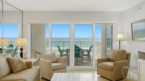 Une pièce comprenant un canapé, des fauteuils, une table basse et une lampe. De grandes portes vitrées offrent une vue sur l’océan.