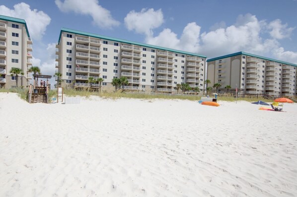 A beachfront hotel with multiple balconies, a sandy beach, and a clear sky. - Sandy Key 326 Third floor -Beachfront view -NO HASSLE CHECK OUT (Perdido Key)