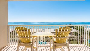 Un balcon avec deux fauteuils Adirondack jaunes et une petite table, donnant sur une plage aux eaux d’un bleu limpide et sur une côte lointaine.