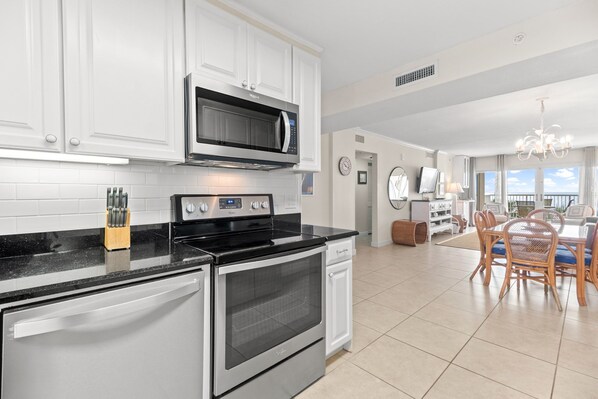 A modern kitchen with white cabinetry, stainless steel appliances, and a dining area with a chandelier. - Sandy Key 327 Third floor -Beachfront view -NO HASSLE CHECK OUT (Pensacola)