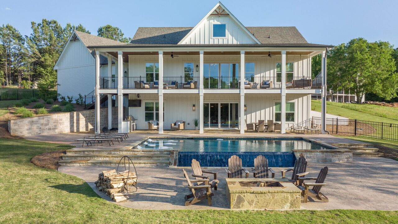 Une maison à deux étages dotée d’une grande terrasse à l’avant, d’une piscine et d’un espace salon extérieur.
