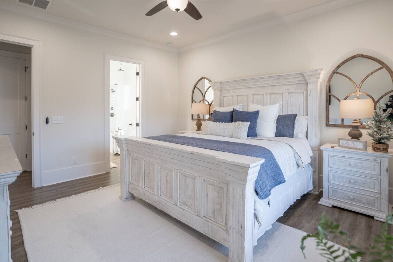 Un dormitorio con una cama blanca, cabecera de madera, mesita de noche con lámpara y un espejo.