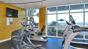 A gym with stationary bikes and treadmills, large windows with a view of the outdoors.